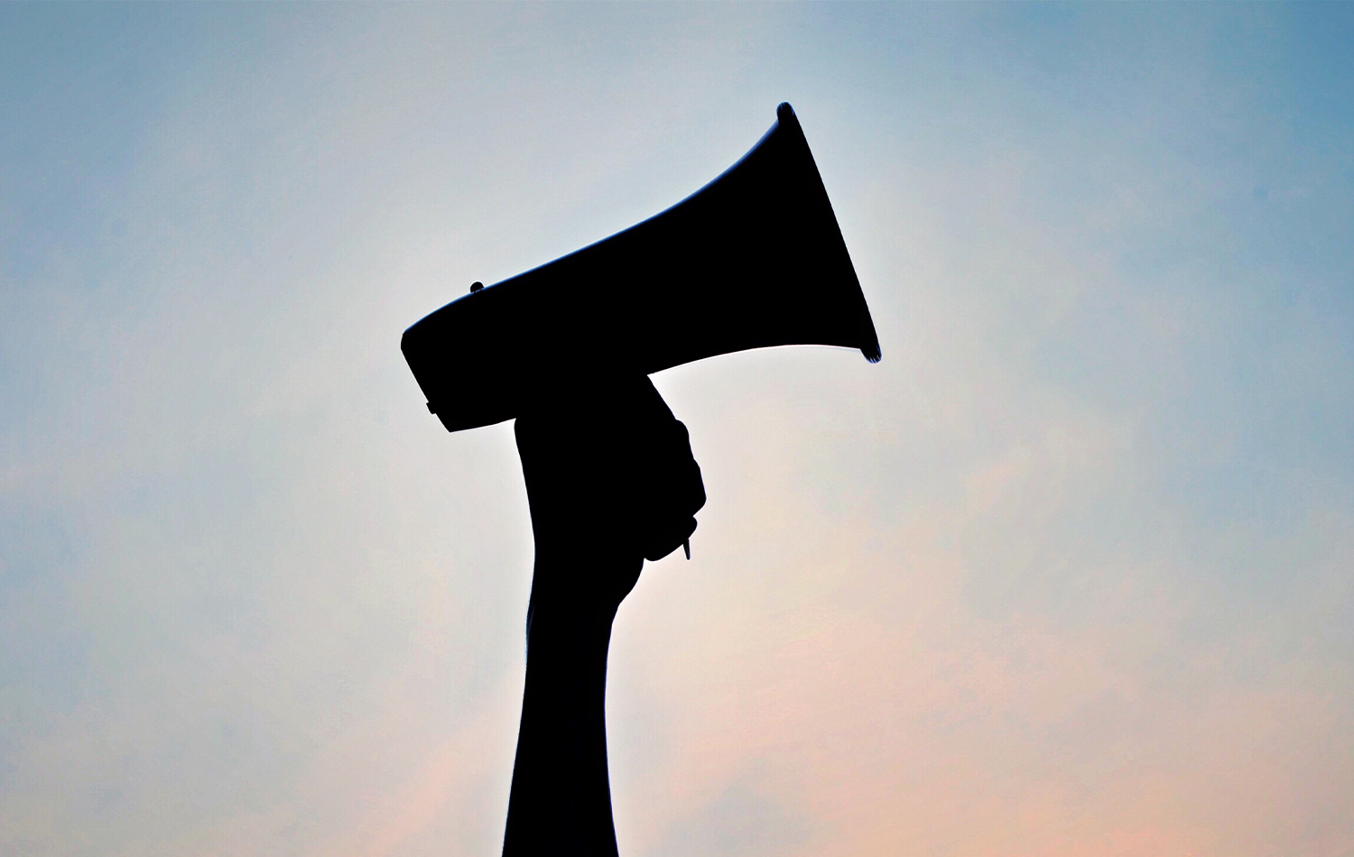 Megaphone held aloft by a person, in silhouette against the sky.