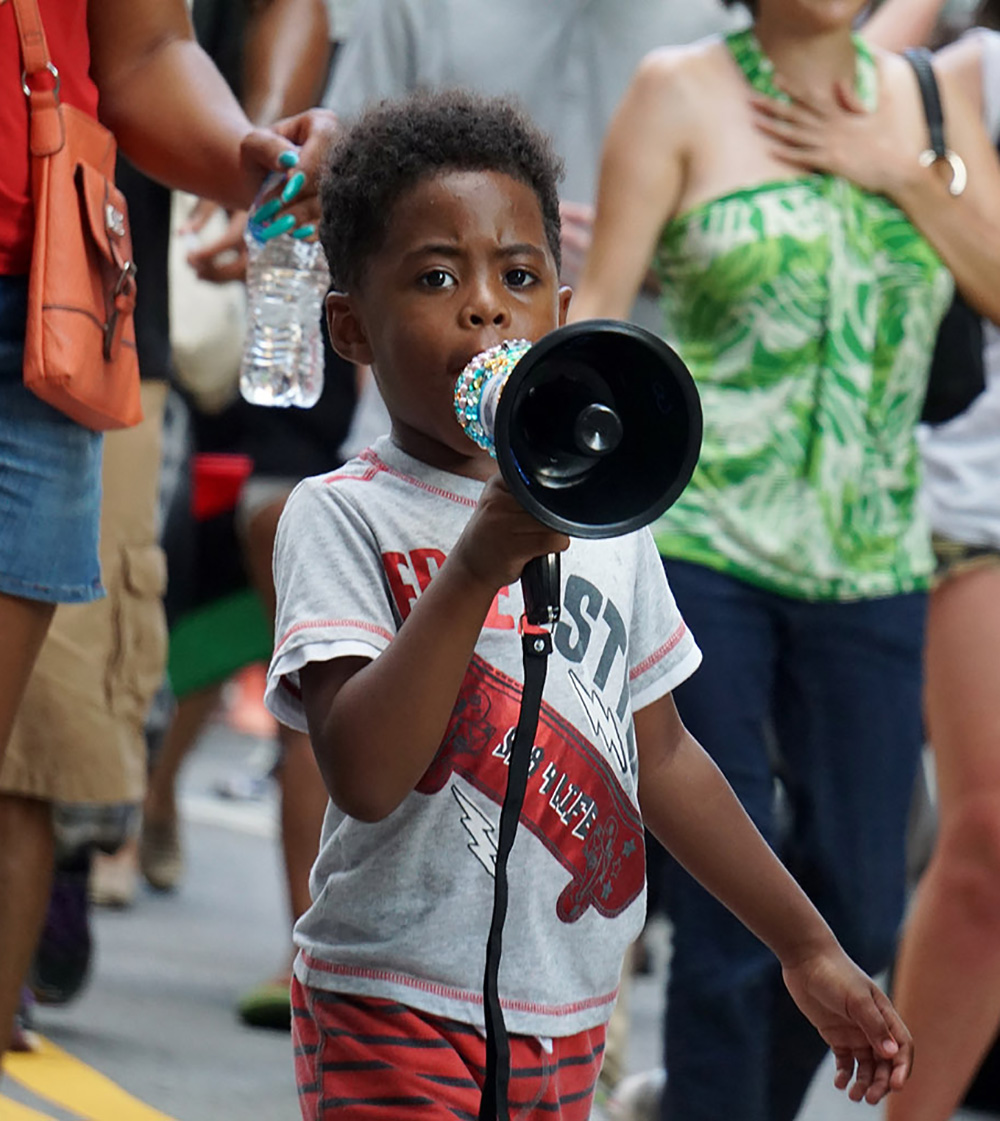 Child protester with bullhorn, walking with other protesters.